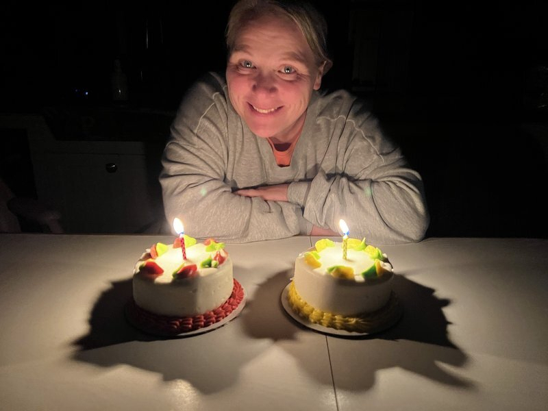 Jody smiling behind two small birthday cakes lit with candles